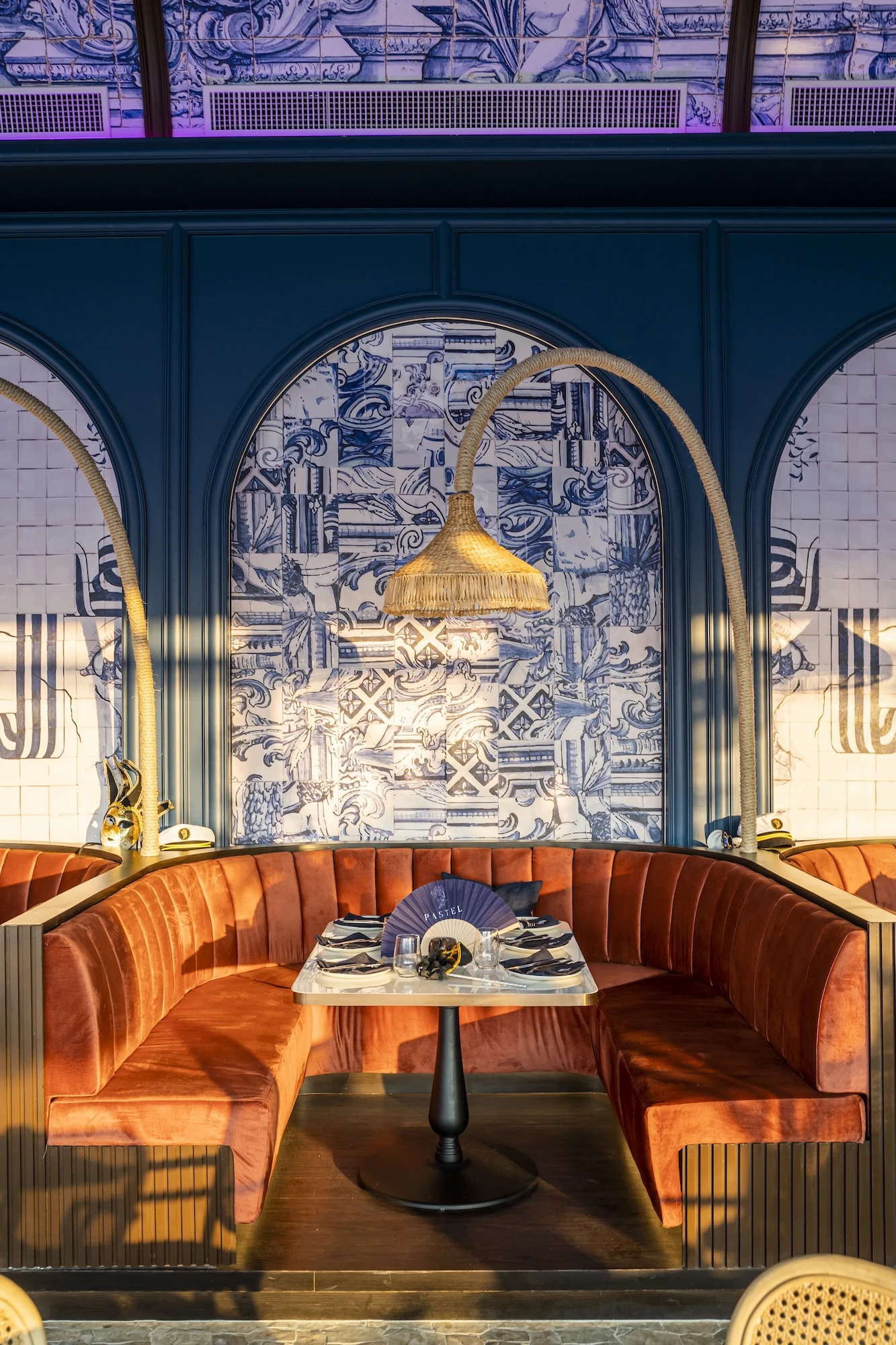 Sunset view of the interior at Pastel Rooftop Bar and Restaurant in Bangkok, featuring red velvet banquettes and intricate wall designs, offering a cozy spot for dining and enjoying cocktails