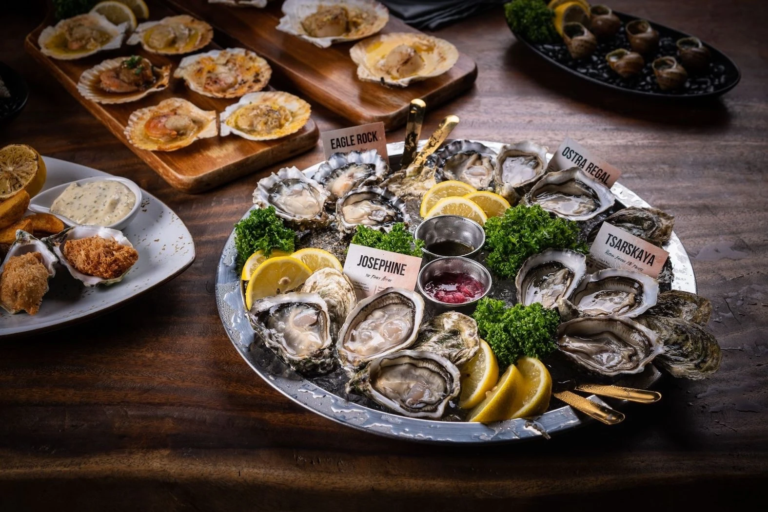 A table where there is an oyster platter and other seafood product at The Oyster Bar Escape in Bangkok. We can see different type of oysters presented with sauces and lemon slices.