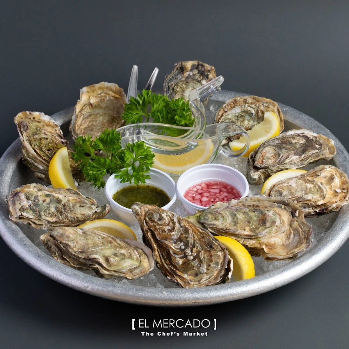 We can see fresh an oyster platter with lemon slices and sauces in El Mercado market restaurant in Bangkok.