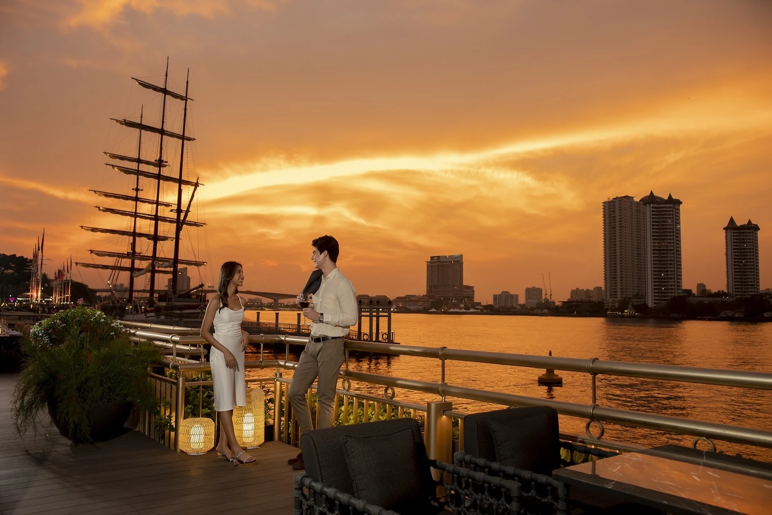 A romantic riverside scene by the Chao Phraya River in Bangkok and golden hues in the sky.