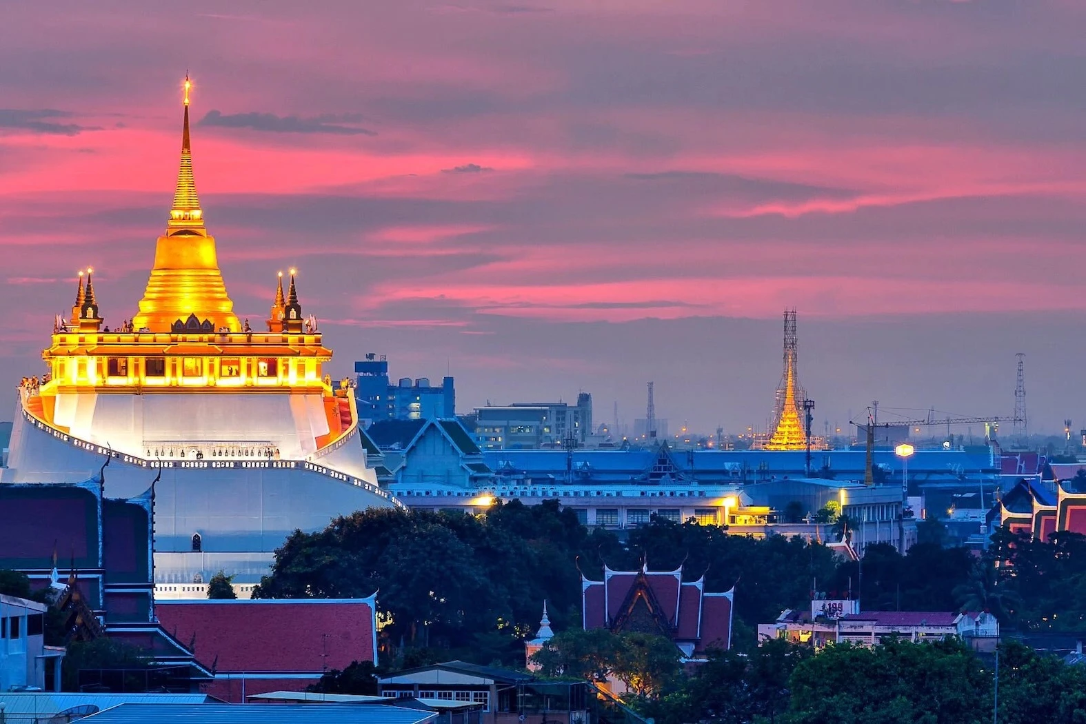 A stunning view of the Golden Mount in Bangkok during sunset, with a vibrant pink and orange sky highlighting the golden glow of the temple