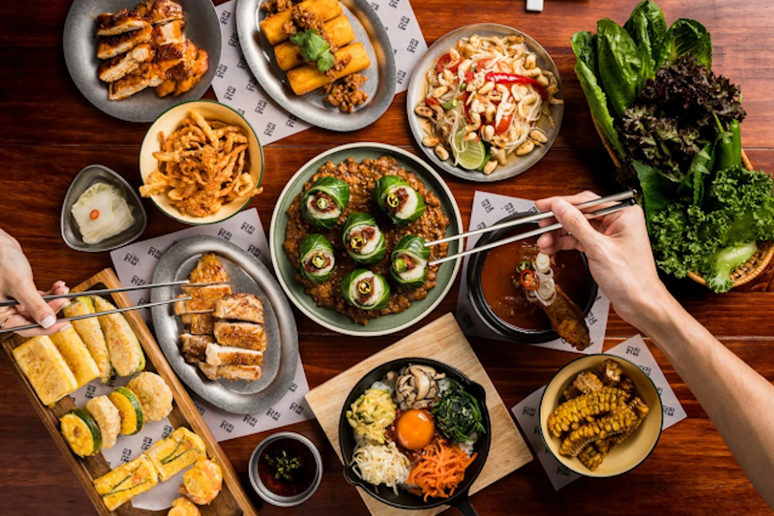 An array of Korean dishes including fried chicken, rolls, and various appetizers, shared in a vibrant atmosphere with chopsticks ready for tasting at Dakjib restaurant